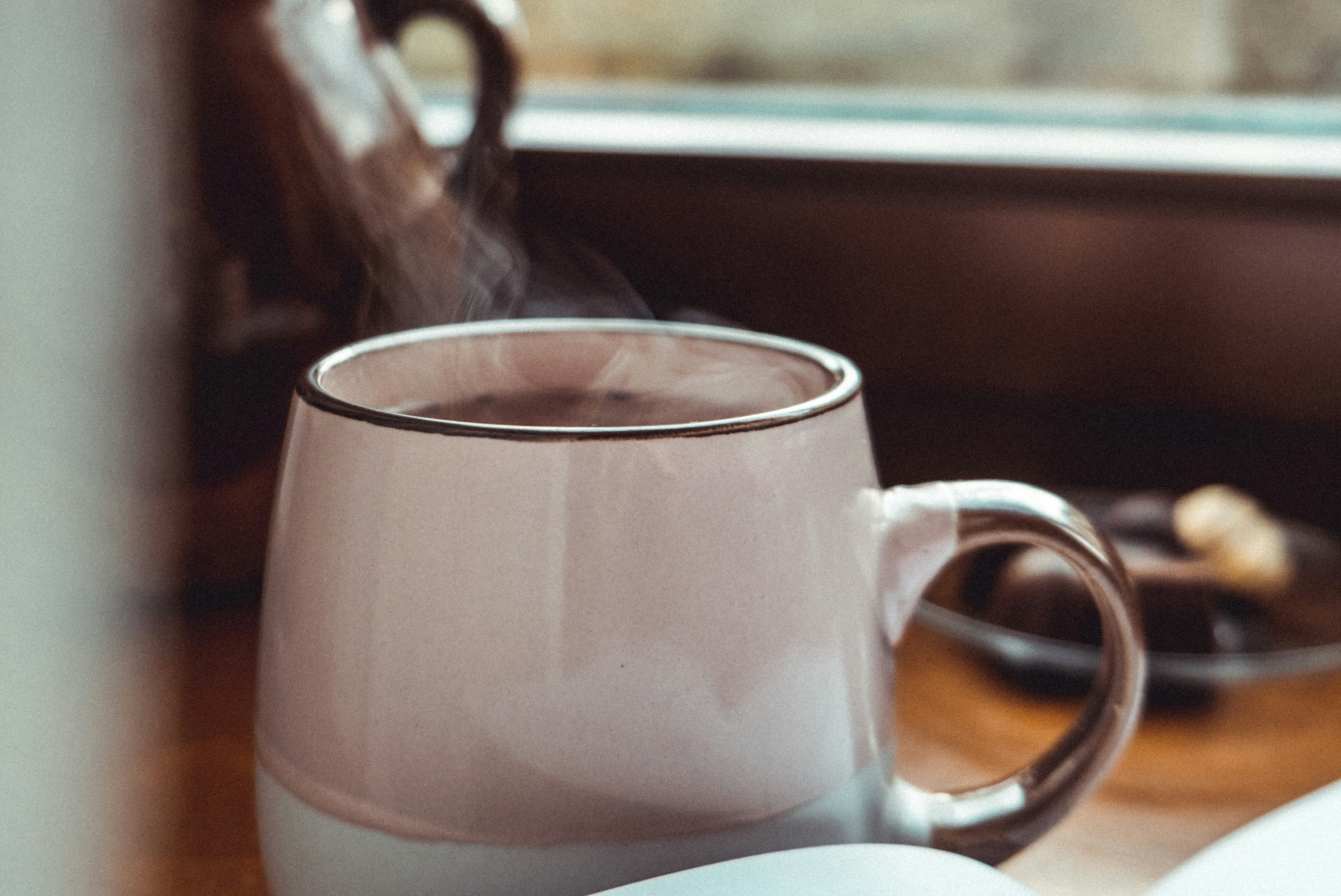 a steaming mug of coffee by a window