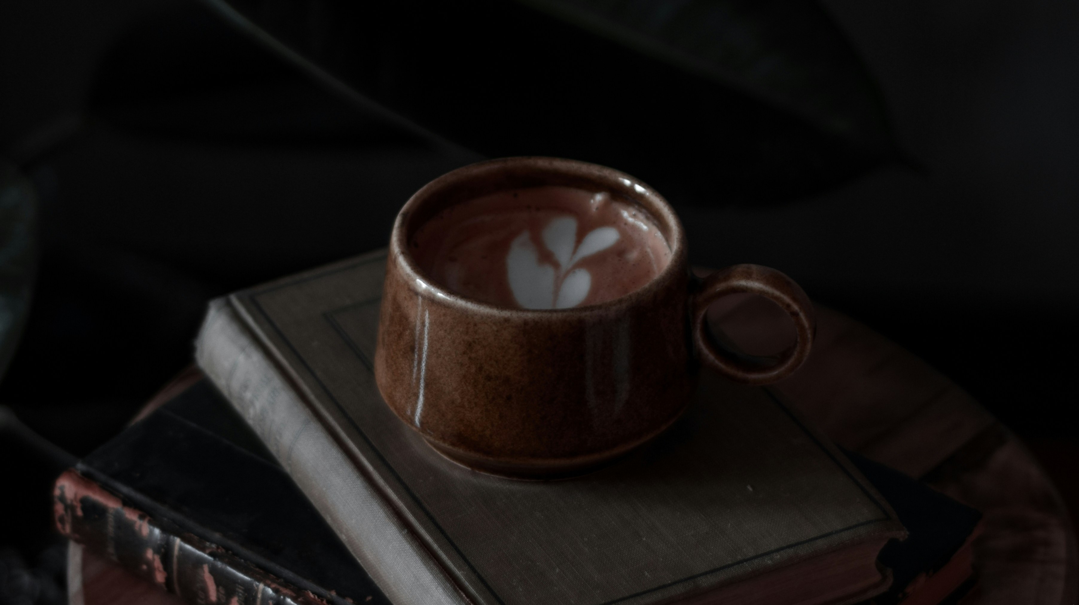 coffee in a cup on books with heart drawn on top layer of foam