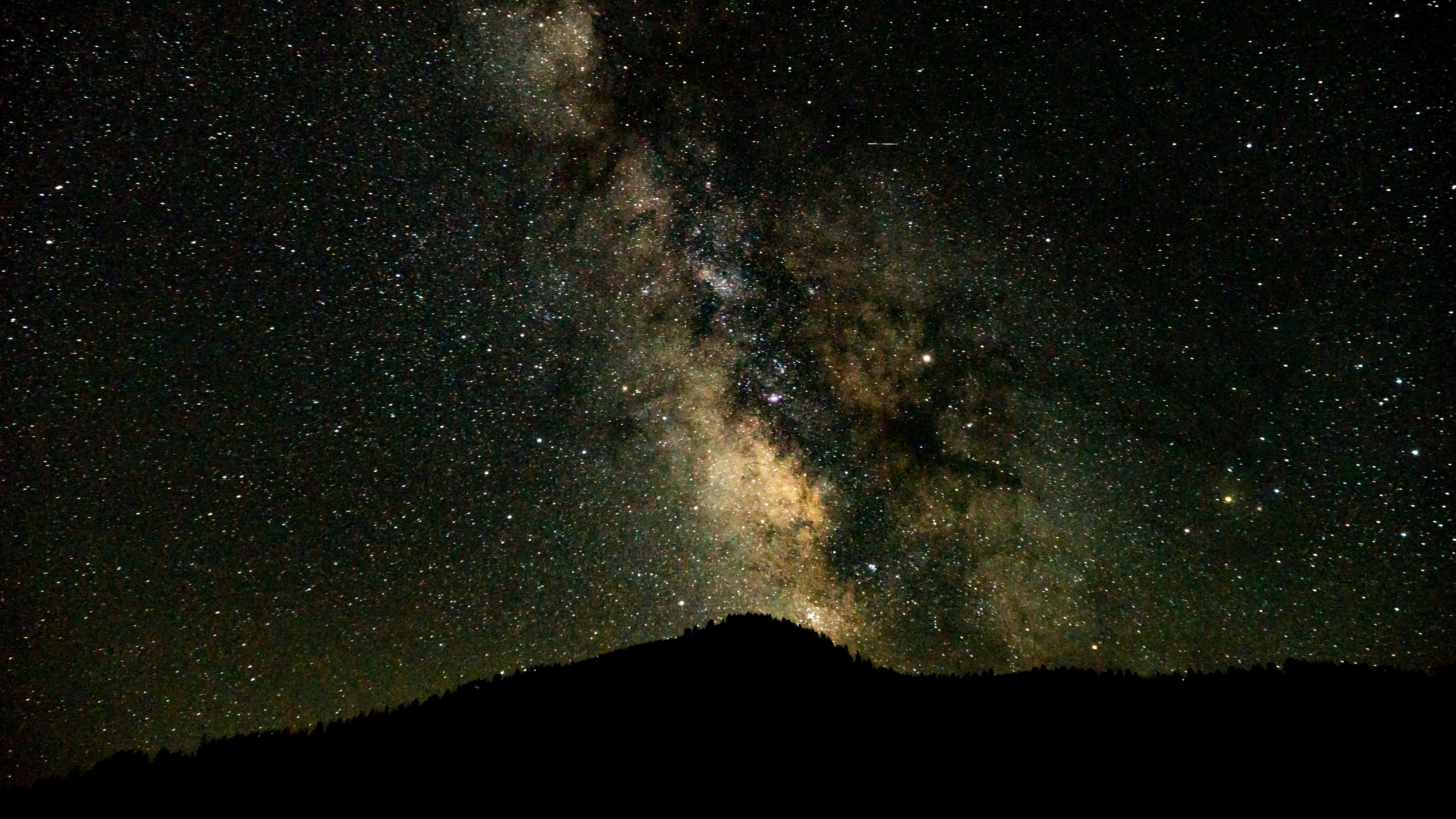 yellowed milky way over dark mountain